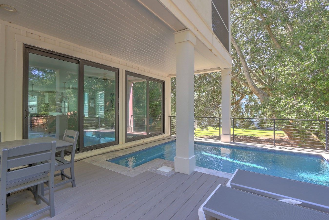 A covered outdoor swimming pool area with a deck, seating, and large windows.