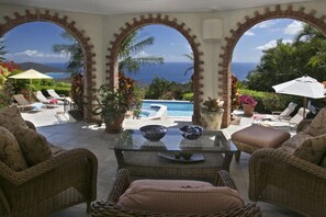 Un patio con mobiliario de mimbre, una mesa de vidrio y una piscina.