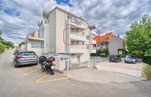 Um edifício residencial com várias andares, varandas, carros estacionados e uma moto.
