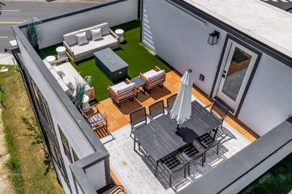 Een terras op het dak met een zithoek, een eettafel en een barbecue.