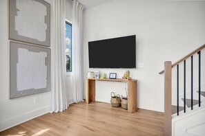 Een moderne woonkamer met een flatscreen televisie die op een houten console tafel is bevestigd, een trap aan de rechterkant en kunstwerken aan de wanden.