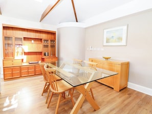 A modern kitchen with wooden cabinets, a glass dining table, and a painting on the wall. - The Mill House Apartment (Lowestoft)