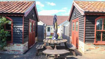 A courtyard with wooden buildings, a central wooden bench, and a metal sculpture.