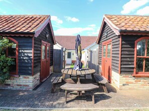 A courtyard with wooden buildings, a central wooden bench, and a metal sculpture. - The Mill House Apartment (Lowestoft)