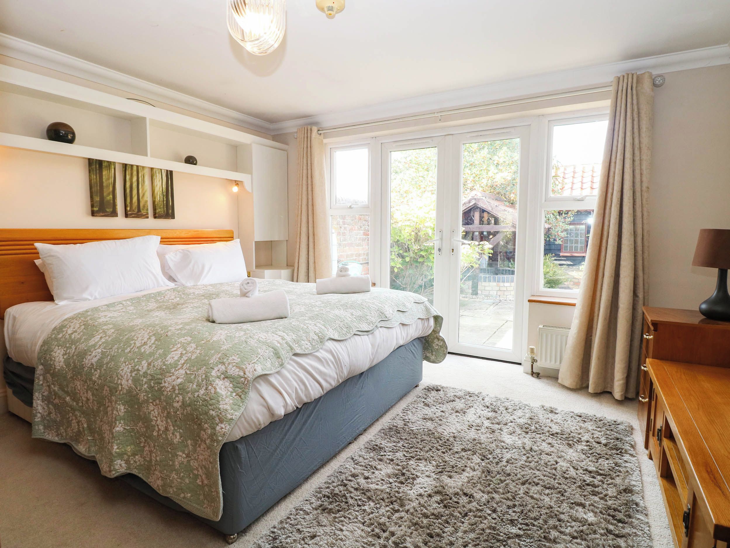 A bedroom with a large bed, a wooden headboard, a bedside table, a lamp, and a view of the outside through a glass door.