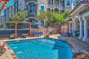 A swimming pool with a stone border, surrounded by outdoor seating and a pergola. - Landing Amazing 2bd, Clubhouse, Gym (San Antonio)