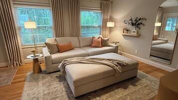 A modern living room with a sofa, ottoman, and a ceiling fan.