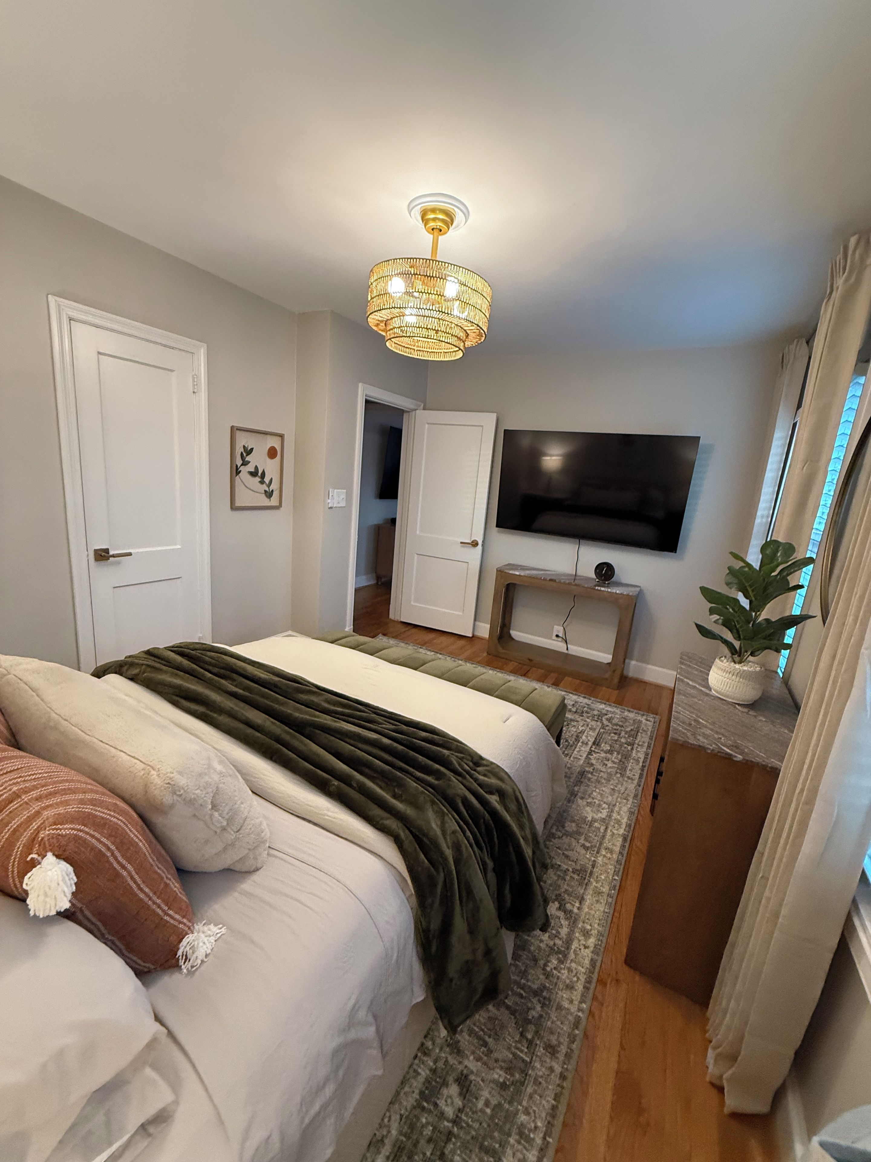 A bedroom with a bed, a television, a plant, and a chandelier.