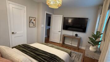 A bedroom with a bed, a television, a plant, and a chandelier.