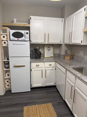 A kitchen with white cabinets, a built-in microwave, a coffee maker, and a framed picture on the countertop. - Luxury Furnished 2BR Condo, RH Design, Monthly Stays (Greensboro)