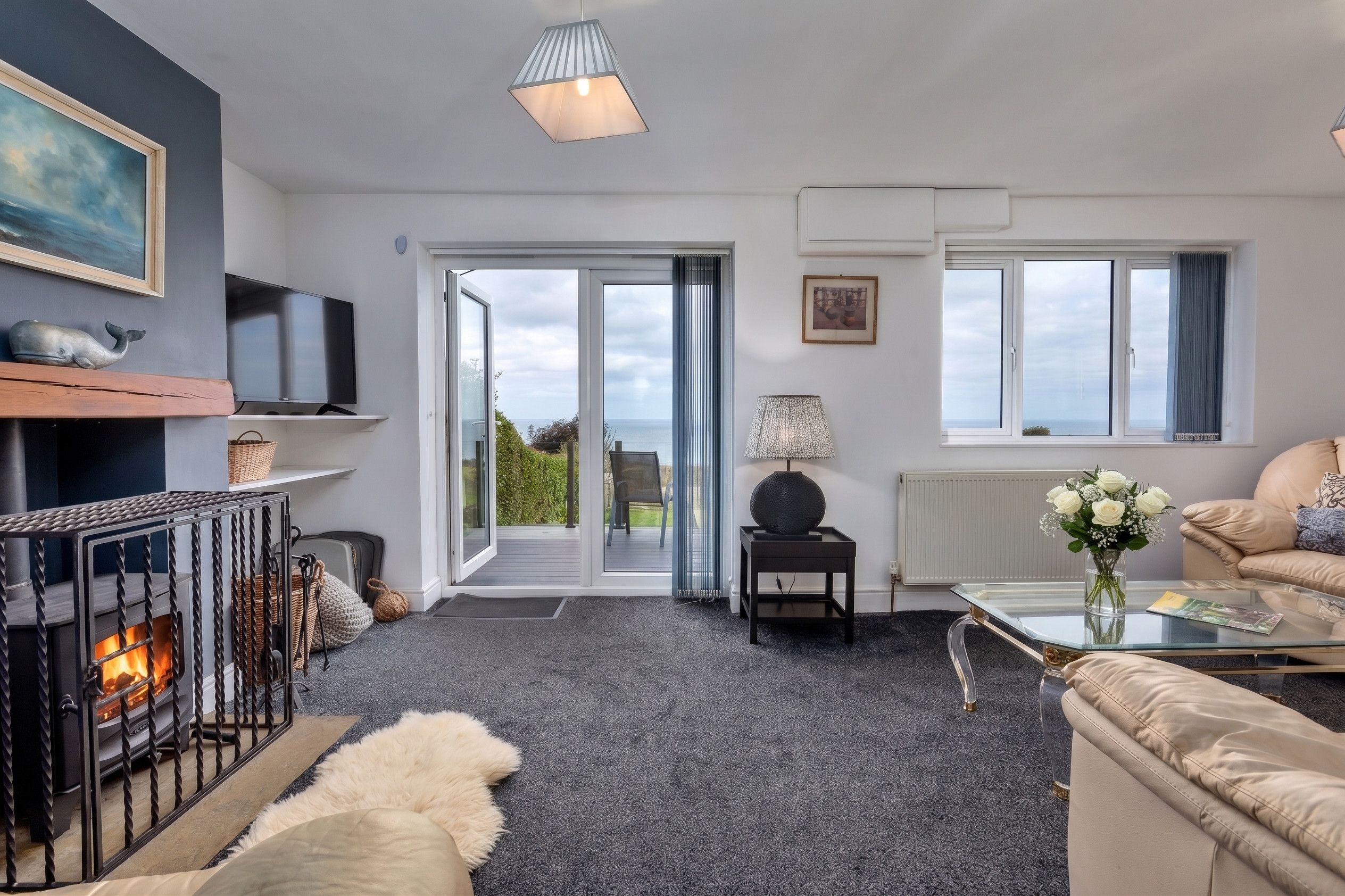 Ein modernes Wohnzimmer mit Kamin, Fernseher, Sofa und Blick ins Freie.