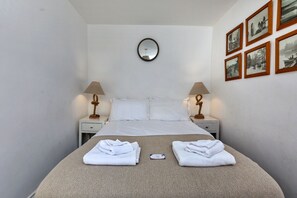 A hotel room with a bed, two bedside tables with lamps, a round mirror above the bed, and a wall with framed pictures. - Ammonite Cottage, Sea Views (Port Mulgrave)