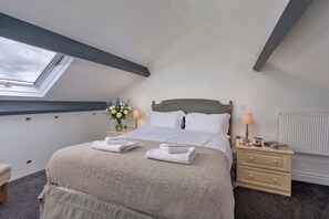 Ein Schlafzimmer mit Dachfenster, einem Bett mit weißer Bettwäsche, einem Nachttisch mit Lampe und einer Heizung.