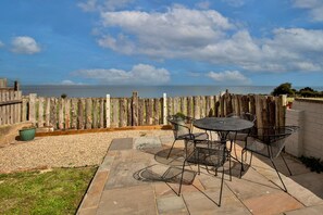 Eine Terrasse im Freien mit Tisch und Stühlen, einem Holzzaun und Blick auf das Meer.