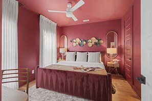 A bedroom with a bed, a ceiling fan, a bedside table with a lamp, a mirror, and a wall decoration. - The Highline | Rooftop Views | 5 Min to Downtown (Nashville)