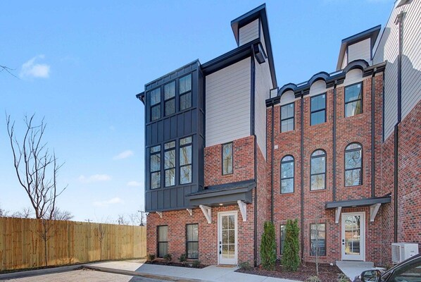 A multi-story residential building with a combination of brick and modern siding, a front porch, and a visible garage door. - The Highline | Rooftop Views | 5 Min to Downtown (Nashville)
