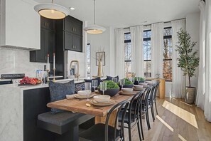 A modern kitchen with dark cabinets, a wooden dining table, and a seating area. - The Highline | Rooftop Views | 5 Min to Downtown (Nashville)