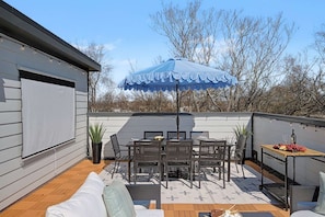 A rooftop patio with a table and chairs, a blue umbrella, and a small cart with food. - The Highline | Rooftop Views | 5 Min to Downtown (Nashville)