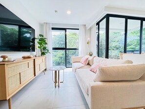 A modern living room with a sofa, a side table, a cabinet, and a large window offering a view of greenery. - Waves & Woods Hideaway (Jaco)