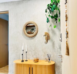 A room with a round mirror, a seahorse decoration, a wooden console table with candles, and a hanging plant. - Waves & Woods Hideaway (Jaco)