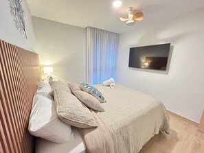 A neatly made bed with multiple pillows, a bedside lamp, a flat-screen TV mounted on the wall, and a window with curtains. - Waves & Woods Hideaway (Jaco)