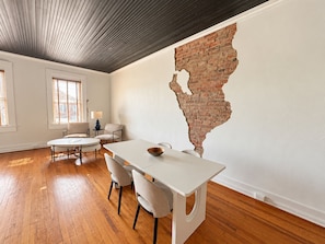A dining area with a white table, four chairs, and a brick wall accent.