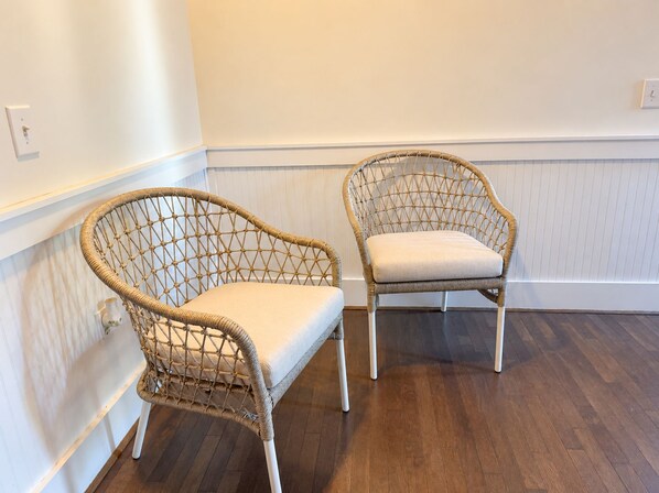 Two wicker chairs with cushions in a room with wooden flooring and white walls.