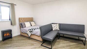 A modern bedroom with a bed, a sofa, a fireplace, and a window with curtains.