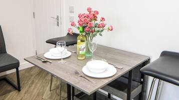 A dining table set with plates, cutlery, a bottle of wine, and a vase with flowers.
