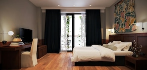 Habitación de hotel con cama, escritorio, silla, televisor y un ventanal con cortinas.