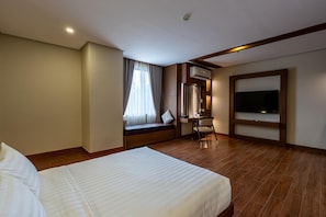 A hotel room with a large bed, a desk with a chair, a TV, and a window with curtains.