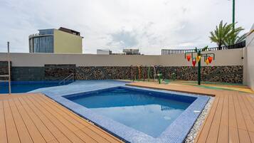 A swimming pool with a tiled edge, surrounded by a wooden deck.