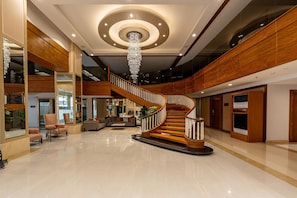 A spacious lobby with a grand staircase, polished floors, and modern lighting fixtures.