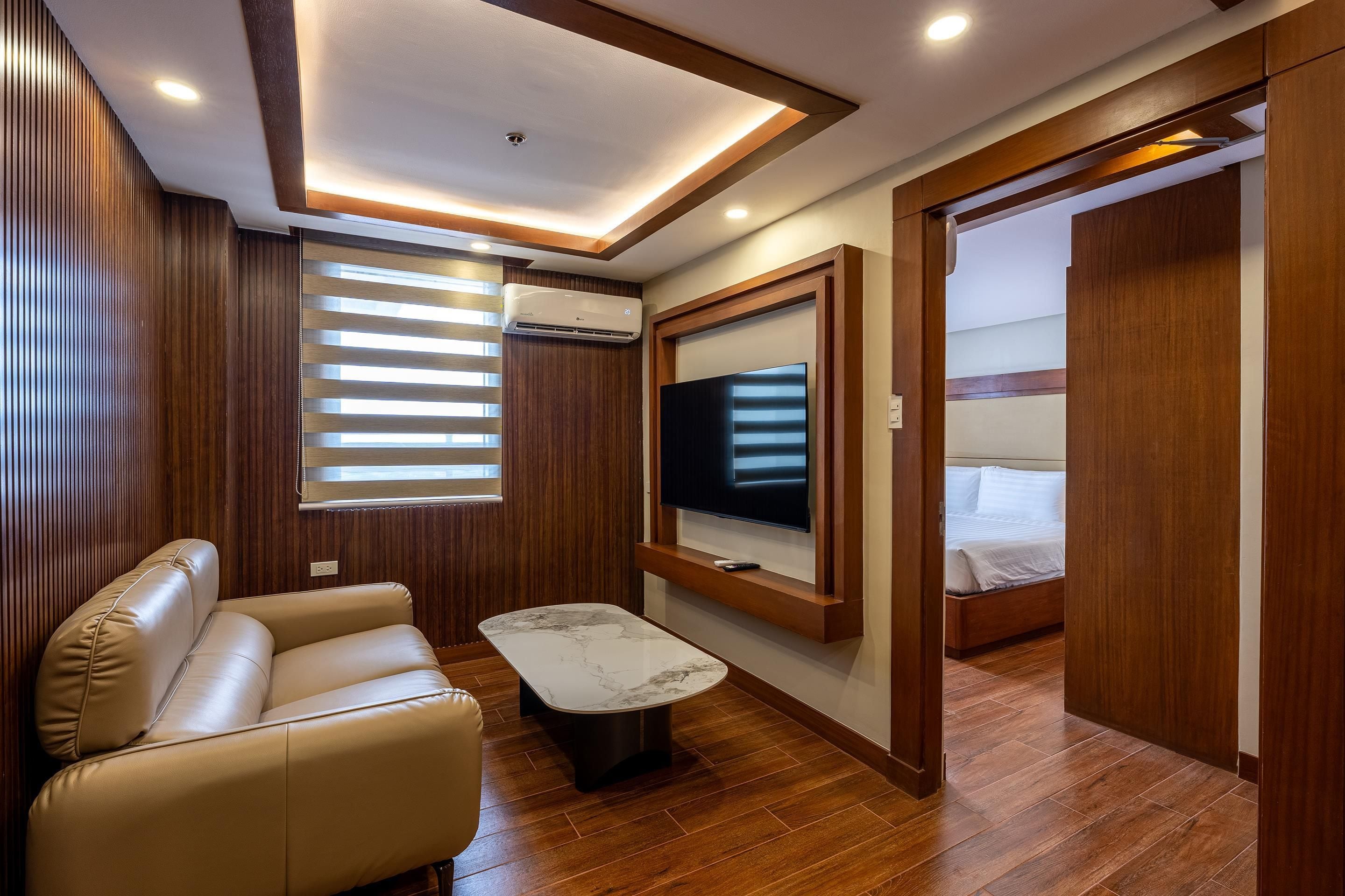 A modern bedroom with a wooden floor, a sofa, a TV mounted on the wall, and a bed.