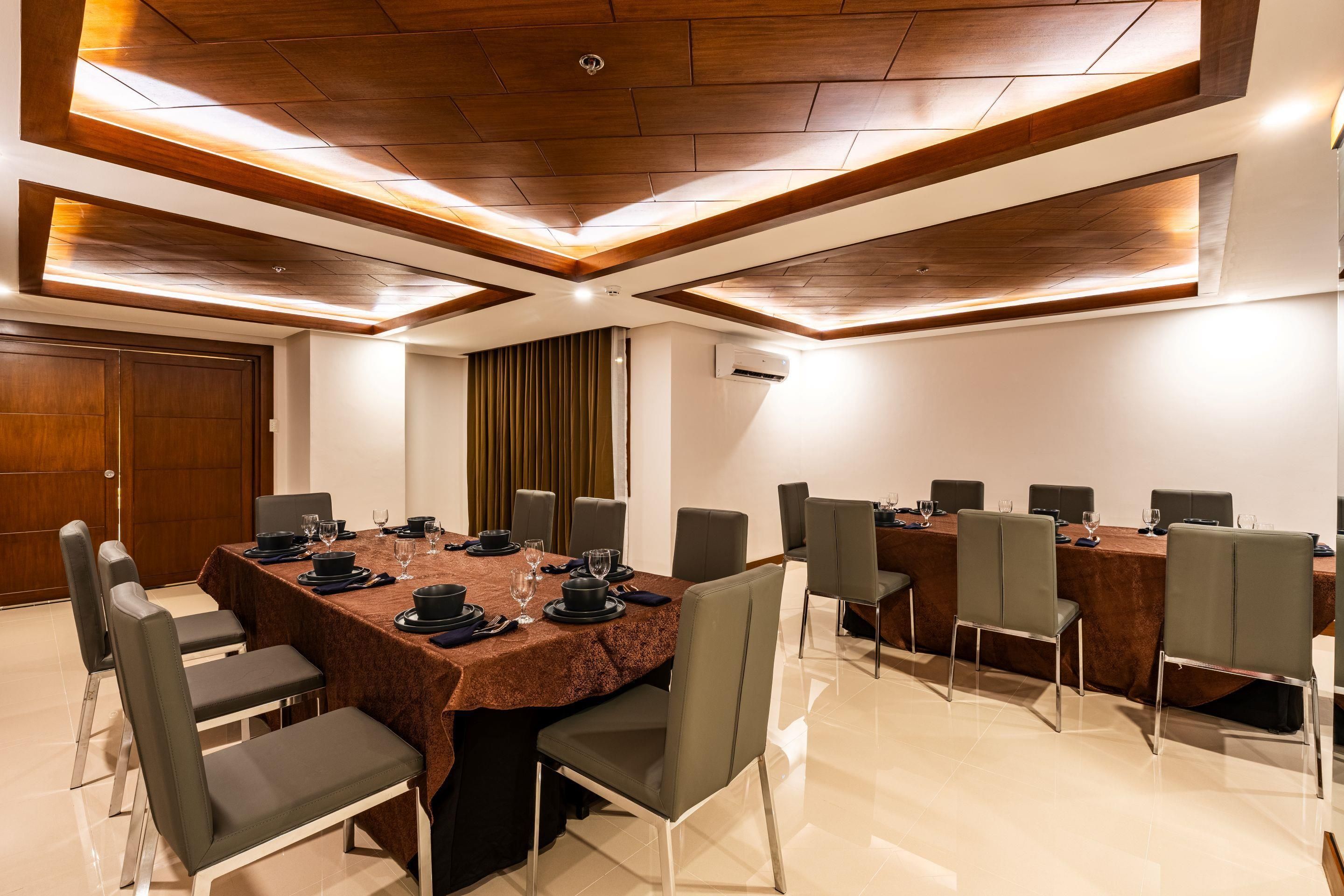A conference room with a long table, chairs, and a ceiling with wooden panels and recessed lighting.