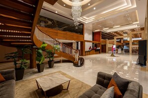 A spacious lobby with a wooden staircase, a reception desk, and a seating area with a coffee table.