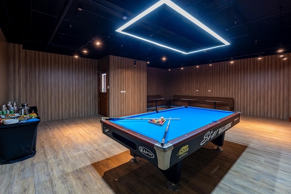 A pool table with a Star Billiards logo, surrounded by wooden walls and a dark ceiling with a geometric light fixture.