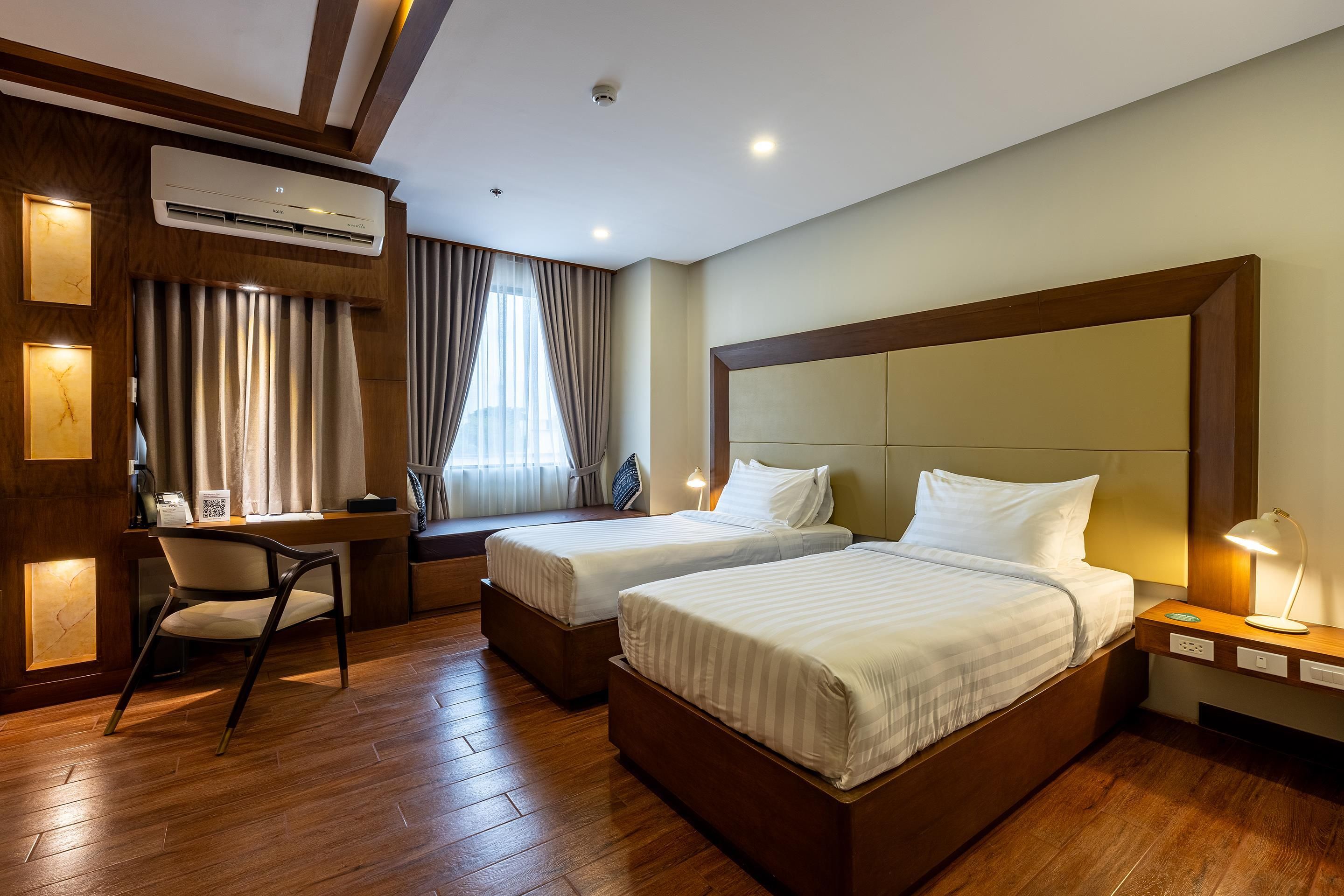 Une chambre d’hôtel avec deux lits, un bureau, une chaise et un appareil de climatisation.