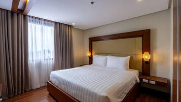 A hotel room with a large bed, wooden headboard, two bedside lamps, and a window with curtains.