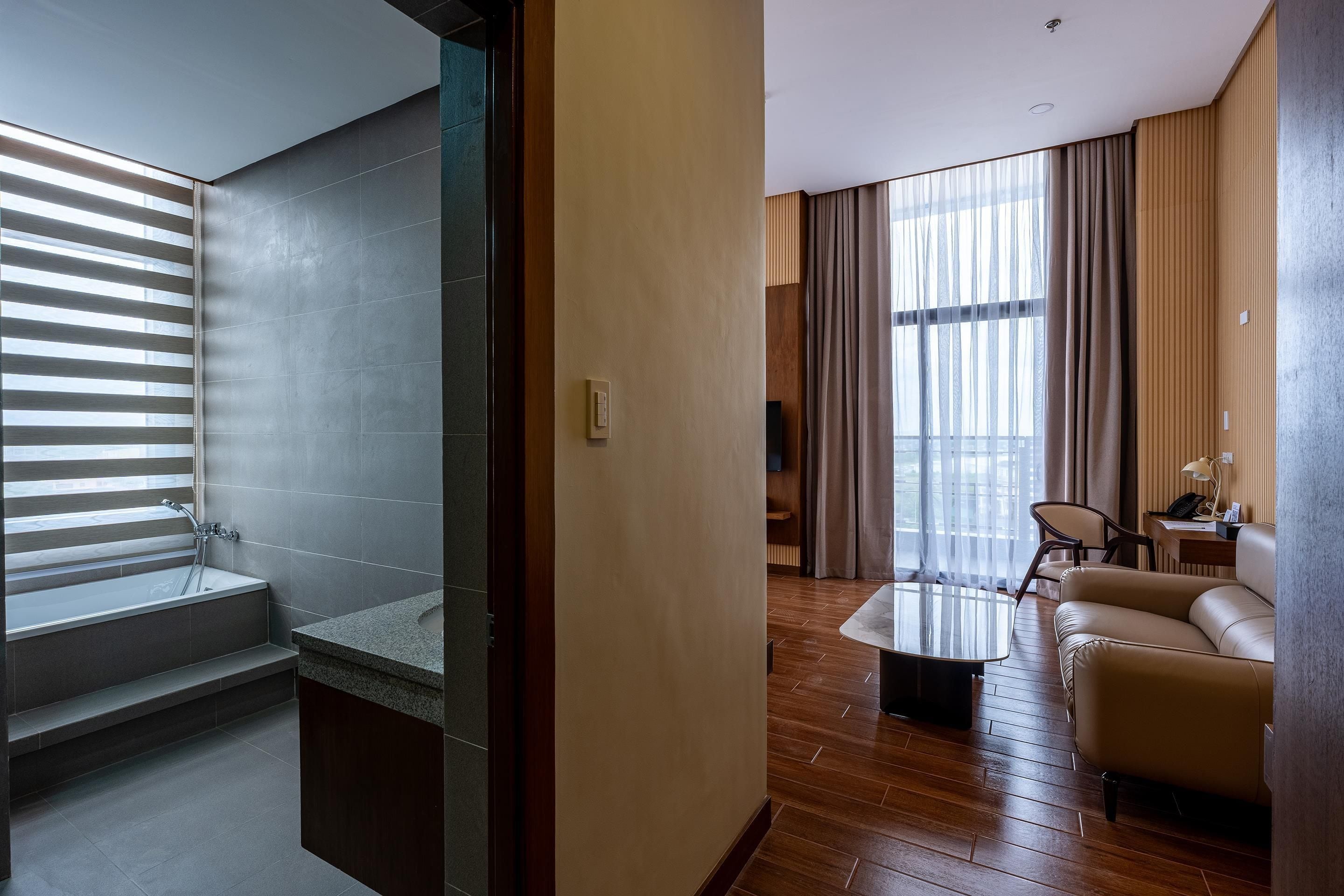 A modern hotel room with a shower, a sofa, a coffee table, and a large window with curtains.