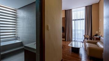 A modern hotel room with a shower, a sofa, a coffee table, and a large window with curtains.