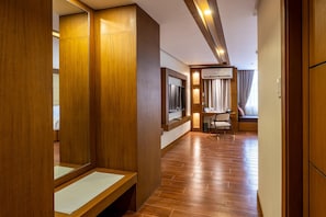 A hotel room with wooden paneling, a large mirror, a flat-screen TV, a desk with a chair, and a window with curtains.