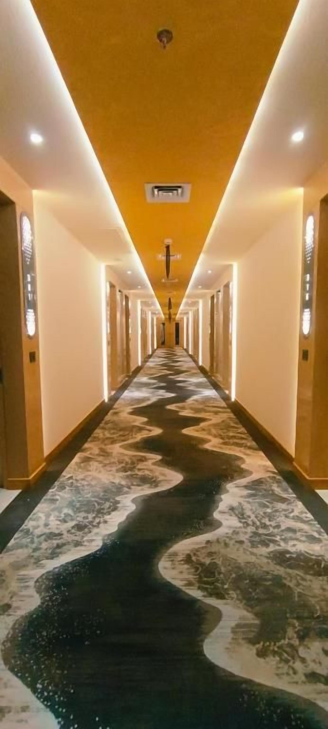 Un pasillo de hotel con un camino central, paredes con lámparas verticales y un techo con iluminación empotrada.