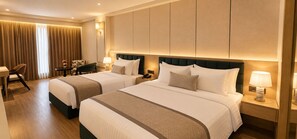 A hotel room with two beds, a desk, a chair, and a lamp.