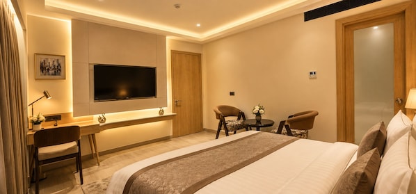 A hotel room with a bed, desk, chairs, and a TV.