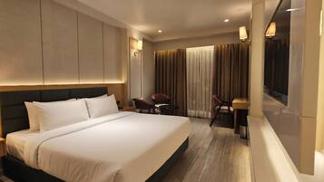 A hotel room with a large bed, a desk, two chairs, and a window with curtains.