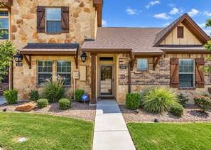 A two-story stone house with a stone facade, a front door, and a small front yard with landscaping. - Howdy House | Private Party Deck • 2.5 Miles to A&M (College Station)