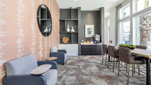 A modern living room with a sofa, coffee table, and dining area with chairs. There is a kitchen area with a coffee machine and a refrigerator. - Landing Amazing 1BD in Whitestone (Fort Worth)