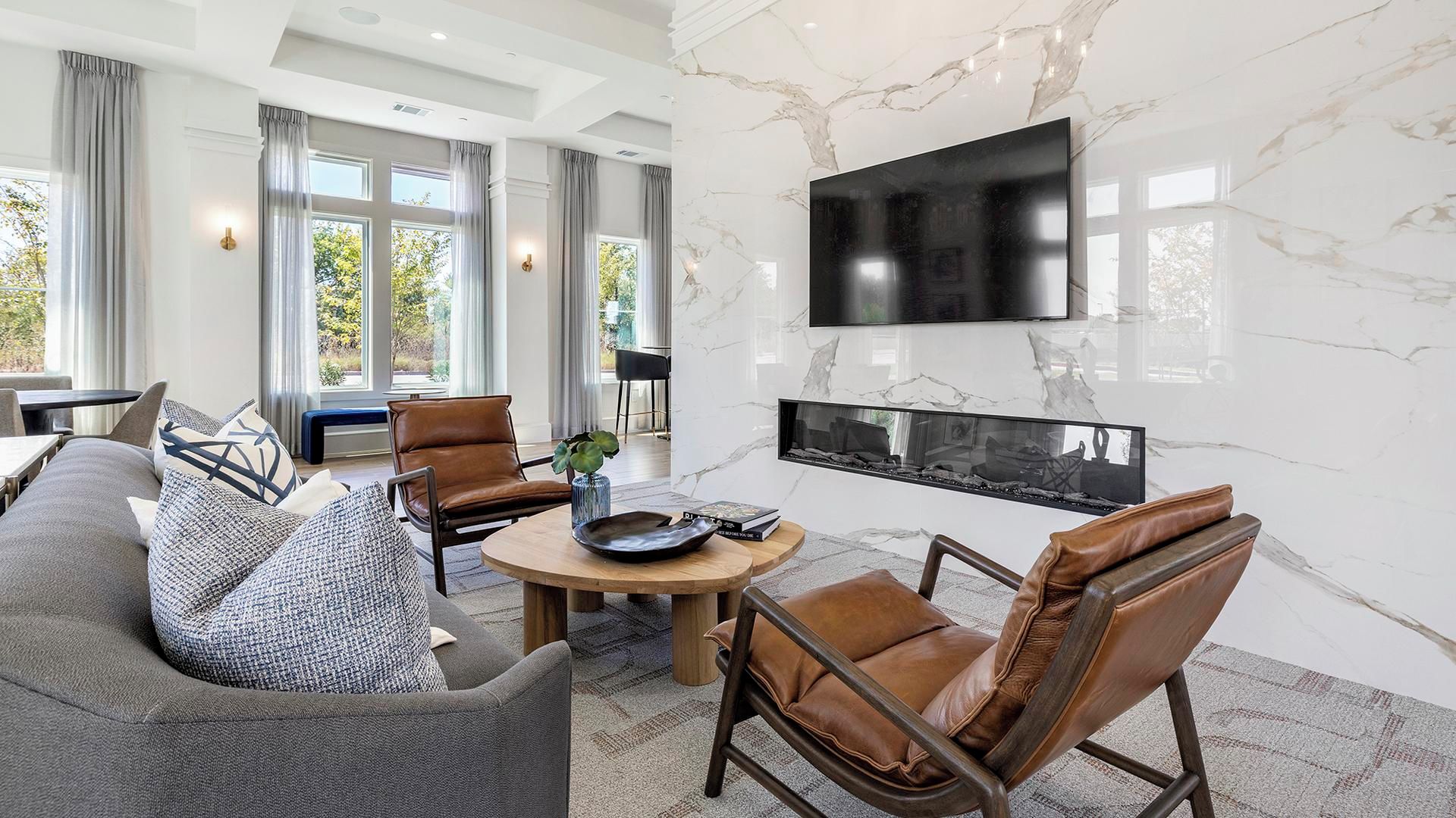 A modern living room with a fireplace, leather chairs, a sofa, and a flat-screen TV mounted on the wall.