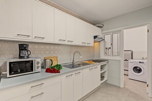 Een moderne keuken met witte kasten, een ingebouwde magnetron, een koffiezetapparaat en een wasmachine in de aangrenzende kamer.